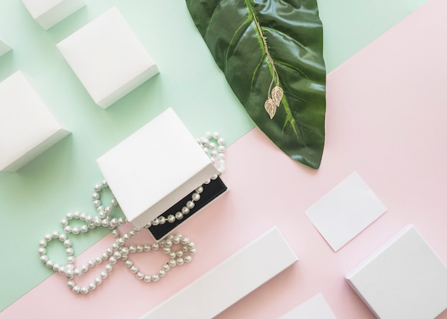 Overhead view of pearl necklace and golden earrings with white boxes on paper background