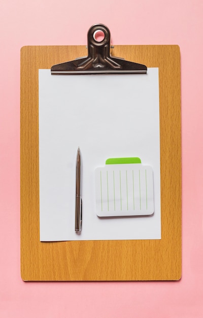 Free photo an overhead view of pen and notepad on blank paper over wooden clipboard against pink background