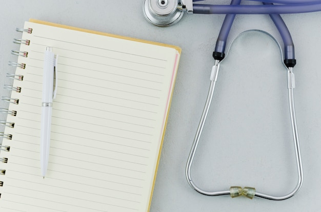 An overhead view of pen over spiral notebook and stethoscope on grey background