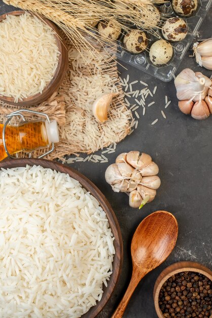 Overhead view of perfect long rice brown bowls on nude color towel fallen oil bottle garlics peppers on dark table