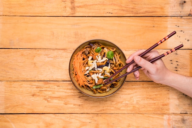 Free photo an overhead view of a person picking the noodles with chopsticks on table