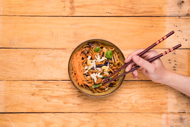 An overhead view of a person picking the noodles with chopsticks on table