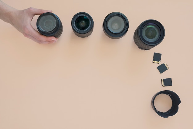 Overhead view of person's hand arranging camera lens; memory card and extension rings over colored background