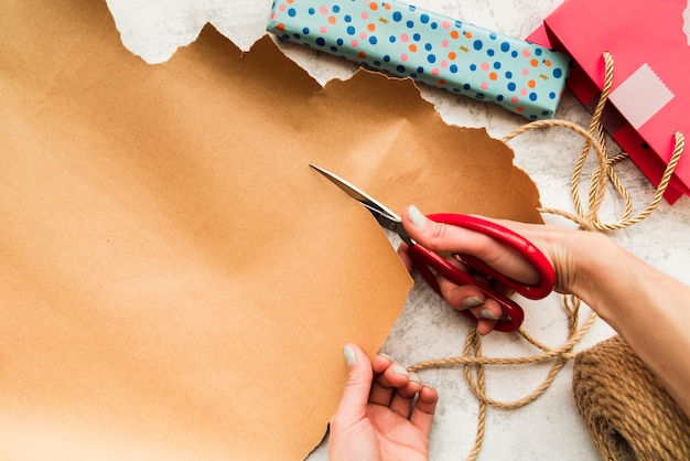 Free photo an overhead view of a person 's hand cutting the brown paper with scissor