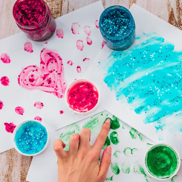 Overhead view of person's hand painting with finger on white paper