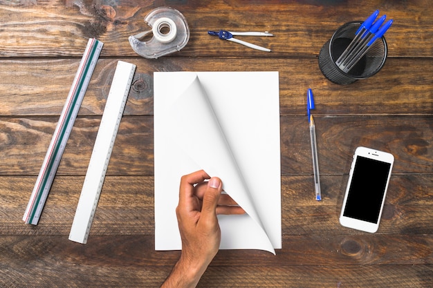 Free photo overhead view of a person turning page with stationery and mobile phone on table