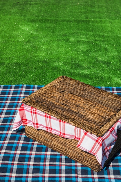 An overhead view of picnic basket on checkered table over green turf