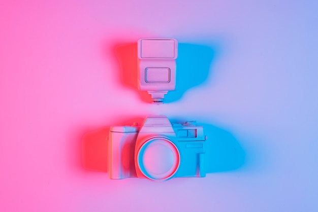 Вид сверху на розовый фотоаппарат и объектив с тенью и синим светом