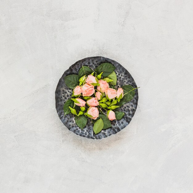 An overhead view of pink flowers on stone tray against concrete backdrop