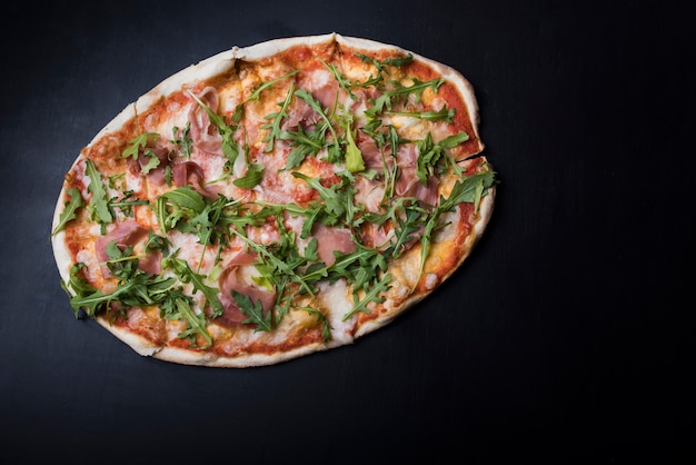 Overhead view of pizza with bacon and arugula on black kitchen counter
