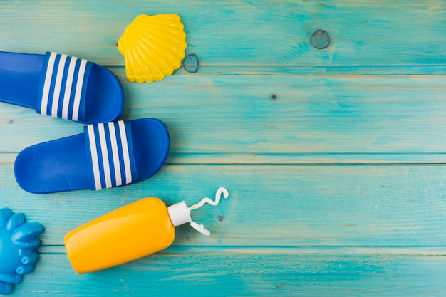 An overhead view of plastic yellow scallop; flip flops and sunscreen lotion bottle on turquoise wooden backdrop