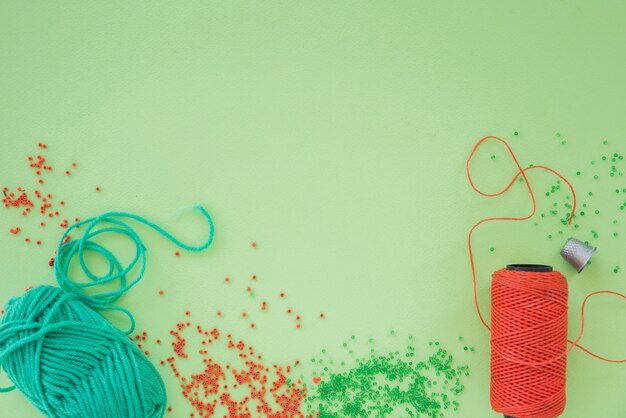 An overhead view of plier; scissor; beads and spool on green backdrop