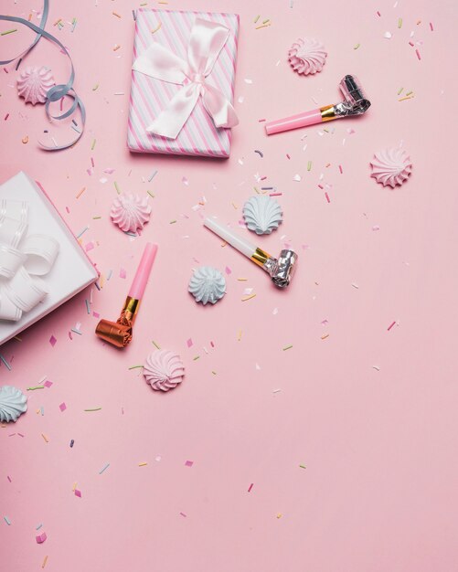 Overhead view of presents; sprinkle; party horn and candies on pink backdrop