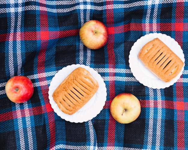 An overhead view of puff pastry on white plate with red apples over blanket