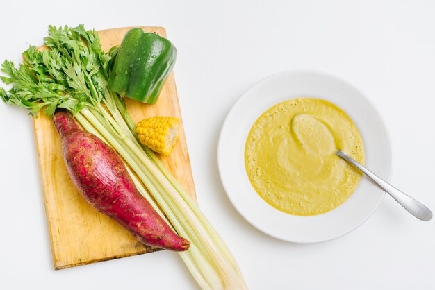 Overhead view of pumpkin puree near raw vegetables on white background