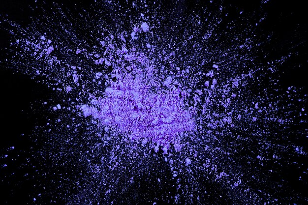 Overhead view of purple color exploding on dark surface