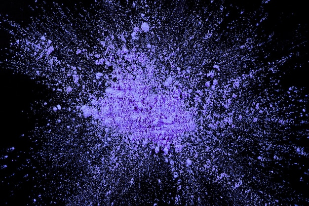 Overhead view of purple color exploding on dark surface