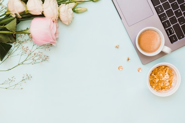 An overhead view of pushpin bowl; coffee cup; flowers and laptop on colored background