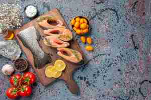 Foto gratuita vista dall'alto di pesce crudo fette di limone verdi pepe sul lato destro sul tagliere di legno e fiore sul tavolo colori blu nero