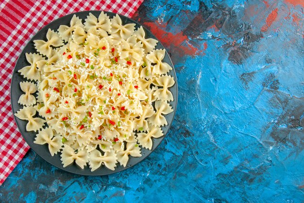 Overhead view of raw Italian farfalle pasta on red stripped towel on blue background