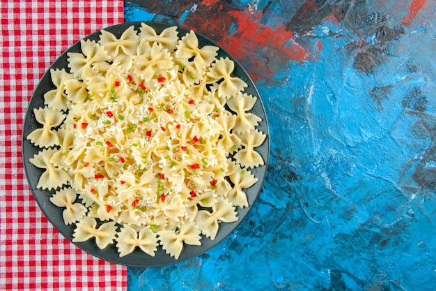 Overhead view of raw Italian farfalle pasta with vegetables on red stripped towel on blue table