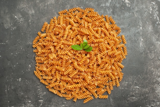 Overhead view of raw Italian pastas with green arranged in circle on gray background