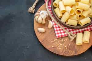 Foto gratuita vista dall'alto di pasta cruda all'interno e all'esterno di una ciotola marrone su asciugamano rosso spogliato garlics riso su tavola di legno rotonda corda su sfondo nero