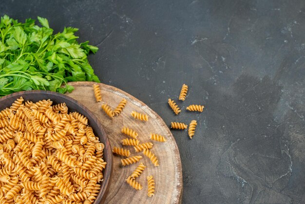 Overhead view of raw pastas inside and outside brown pot green bundle on the right side on dark blue color background