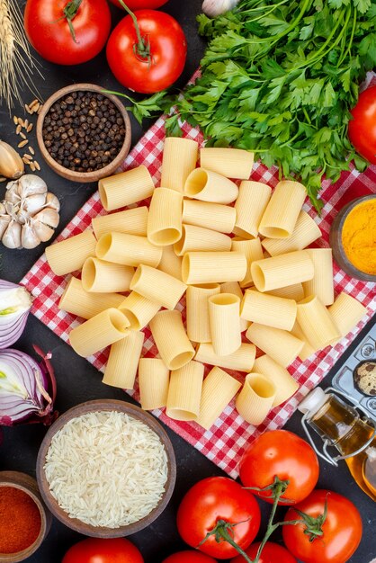 Overhead view of raw pastas on red stripped towel yellow ginger fallen oil bottle fresh vegetables on black table