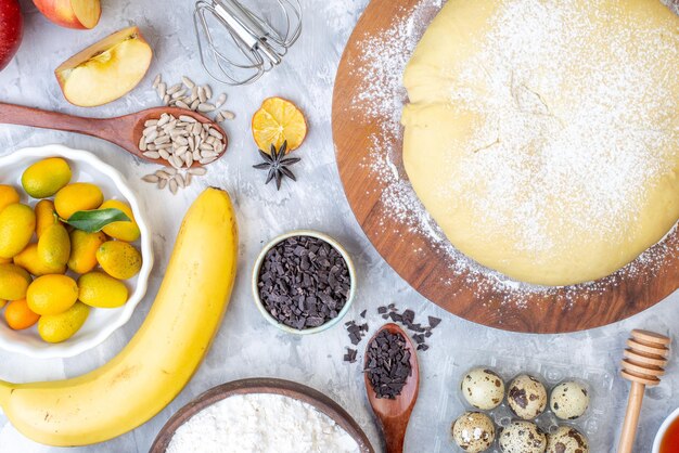 Foto gratuita vista dall'alto della farina di pasticceria cruda su tavola rotonda banana kumquat mele cioccolatini uova su sfondo bianco colorato