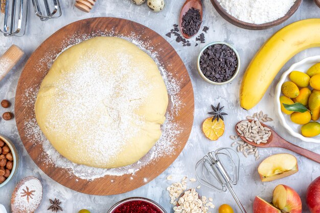 Overhead view of raw pastry on round wooden board grater and set of foods on ice background