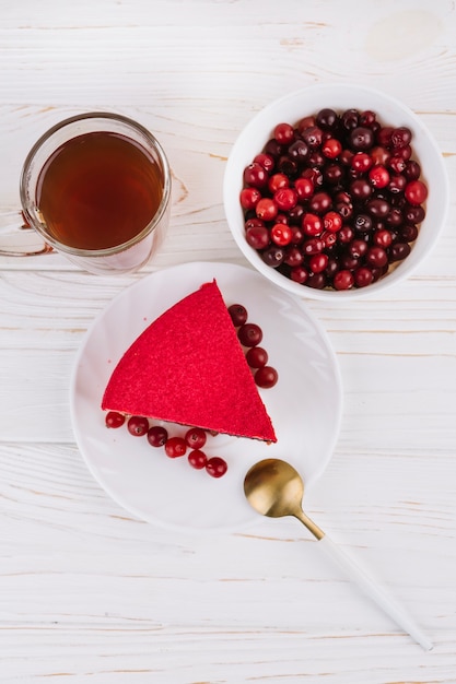 An overhead view of red currant berry cake slice on white plate over the wooden textured backdrop