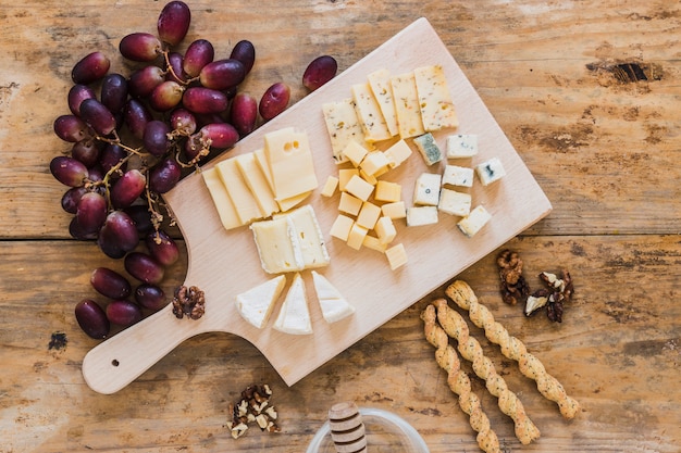 An overhead view of red grapes, variety of cheese, bread sticks on wooden desk