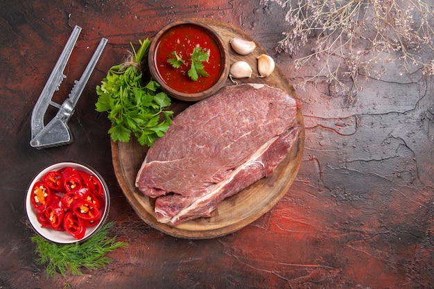 Overhead view of red meat on wooden tray and garlic green ketchup and chopped pepper on dark background