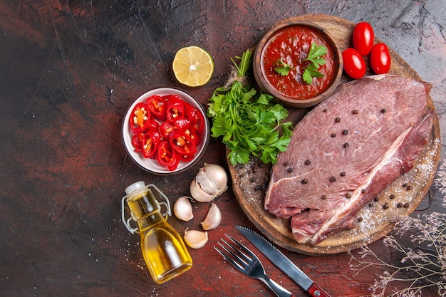 Overhead view of red meat on wooden tray and garlic green ketchup and chopped pepper fallen oil bottle on dark background