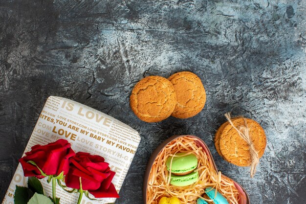 얼음 어두운 배경에 맛있는 마카롱과 쿠키가 있는 아름다운 선물 상자에 있는 빨간 장미의 머리 위