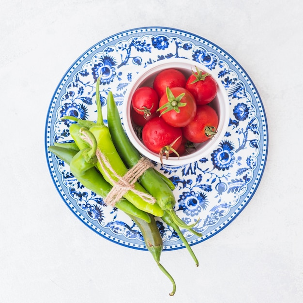 Free photo an overhead view of red tomatoes and bundle of green chilies on ceramic plate