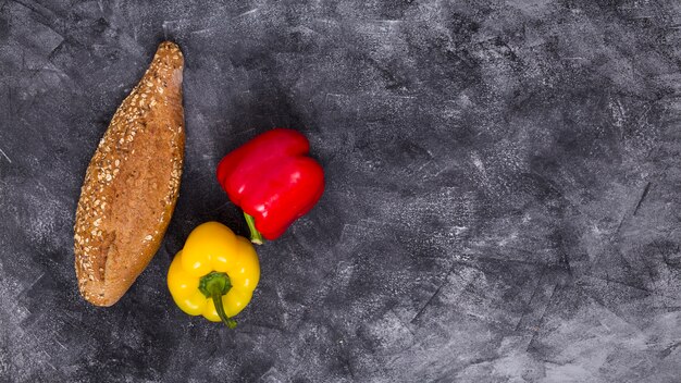 An overhead view of red and yellow bell peppers with loaf of bread against black textured background