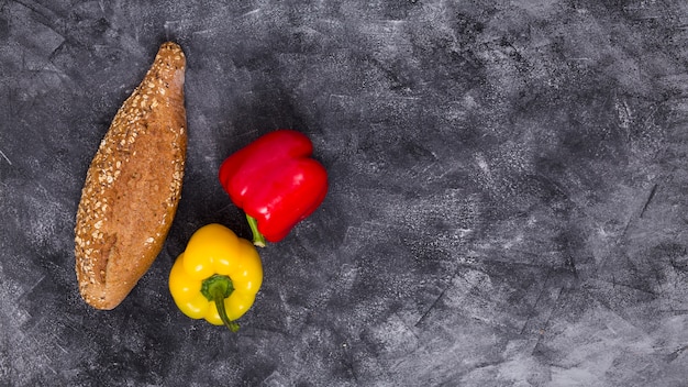 An overhead view of red and yellow bell peppers with loaf of bread against black textured background