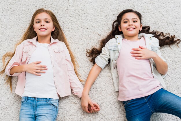 An overhead view of relaxed two girls lying on carpet looking up