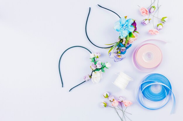 An overhead view of ribbon; artificial flowers; spool for making hairbands on white background