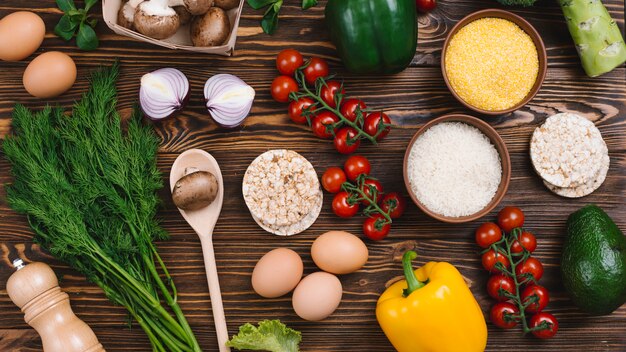 An overhead view of rice grains; polenta; puffed rice cake and vegetables on wooden table