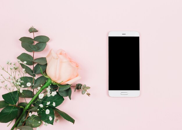 An overhead view of rose flower and gypsophila near the cellphone on pink surface