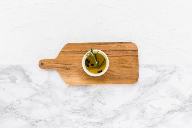 Overhead view of rosemary and black pepper oil in the bowl on serving board