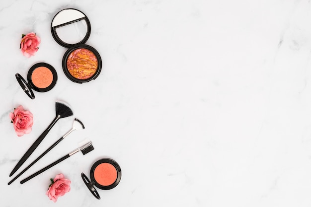 An overhead view of roses with compact face powder and makeup brushes on white background