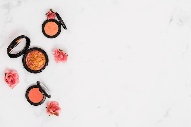 An overhead view of roses with compact face powder on white background