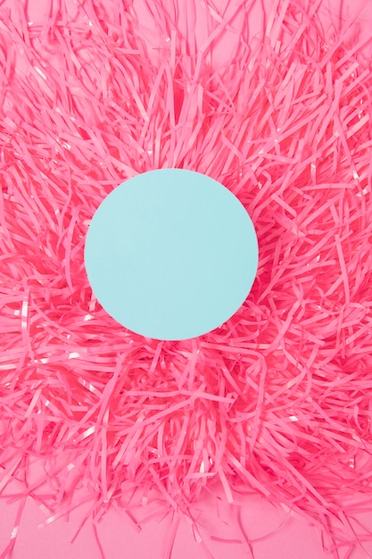 An overhead view of round frame on pom pom against pink background