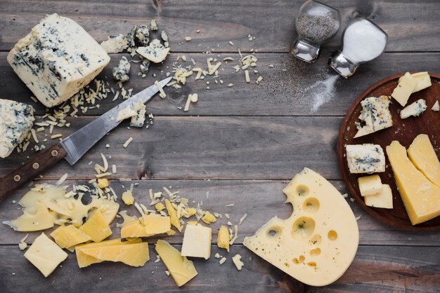 An overhead view of salt and pepper shaker with cheese on wooden desk