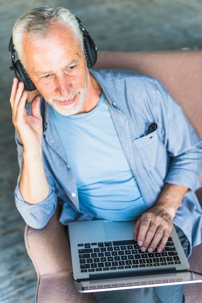Накладные зрения старшего человека, прослушивания музыки на наушники с ноутбуком