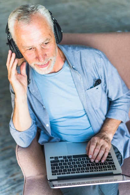 Overhead view of senior man listening music on headphone with laptop